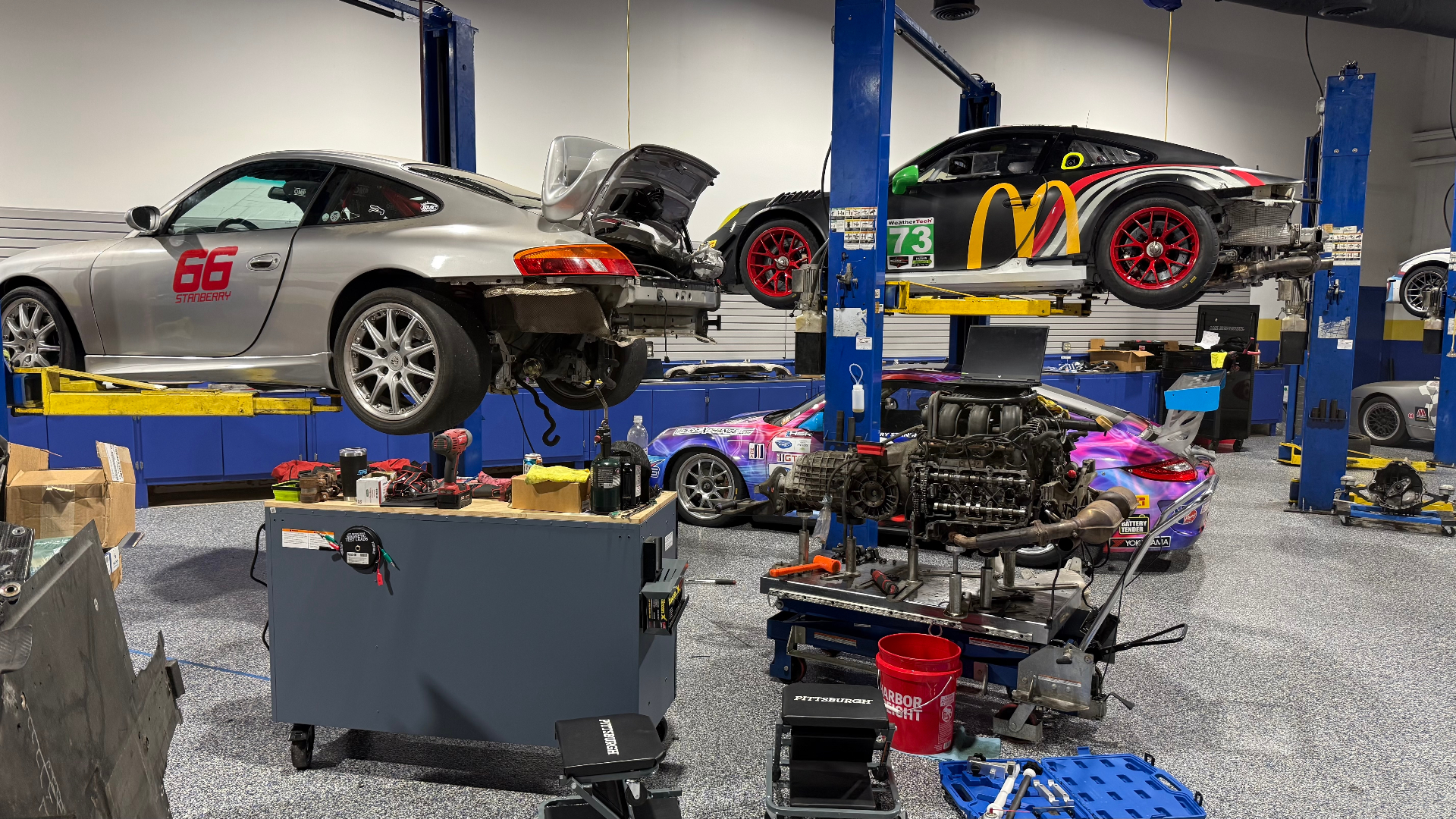 Porsche race cars on lifts and an engine assembly in the DAS Sport workshop