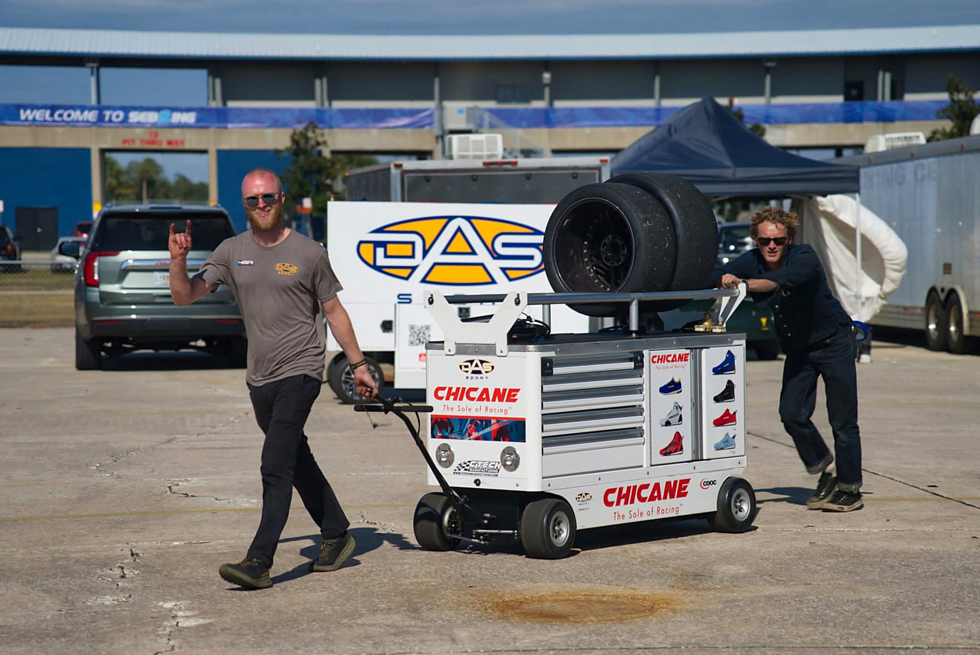 DAS Sport crew rolling a Chicane tool cart and tires through the paddock in front of the DAS Sport transporter