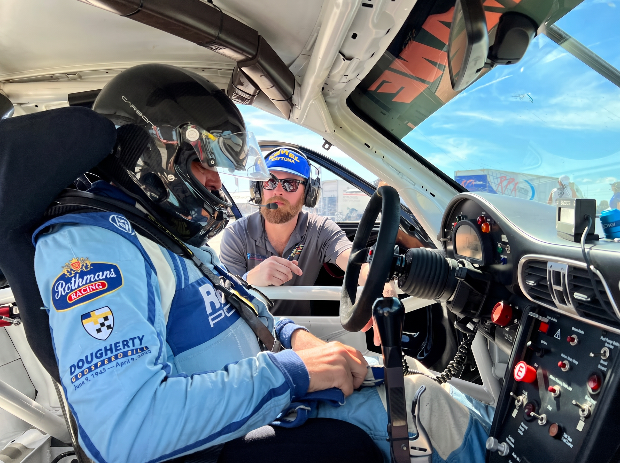 DAS Sport engineer briefing a helmeted driver at the wheel of a Porsche Cup car on grid